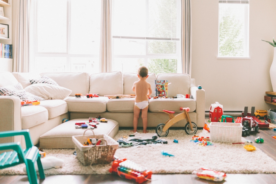 ילד קטן עם טיטול משחק עם צעצועים בסלון מבולגן מלא בצעצועים שמפוזרים על הרצפה.